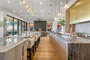 Kitchen with light stone counters, a large island, decorative light fixtures, ceiling fan, and modern cabinets