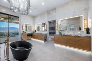 Full bathroom featuring two vanities, a soaking tub, light tile patterned flooring, a large fireplace, and a high ceiling