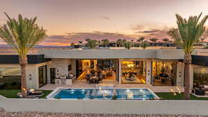 Back of house at dusk with an outdoor kitchen and area to lounge, a patio area, stucco siding, and an outdoor pool