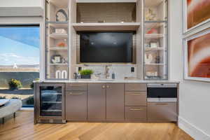 Indoor wet bar featuring beverage cooler, light wood-style flooring, light stone countertops, modern cabinets, and gray cabinets