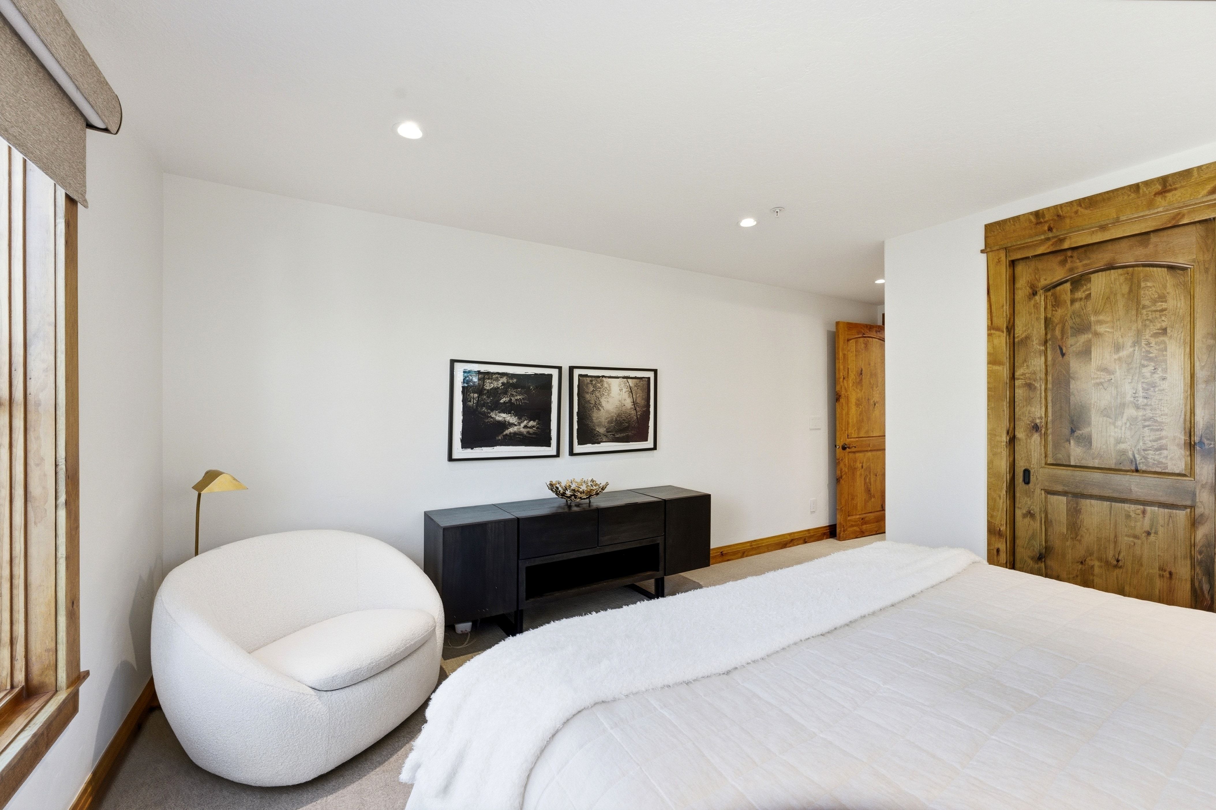 Spacious bedroom featuring light-toned walls, recessed lighting, wood-finish window trim, a wood-finish door with substantial framing, and neutral-toned carpeting