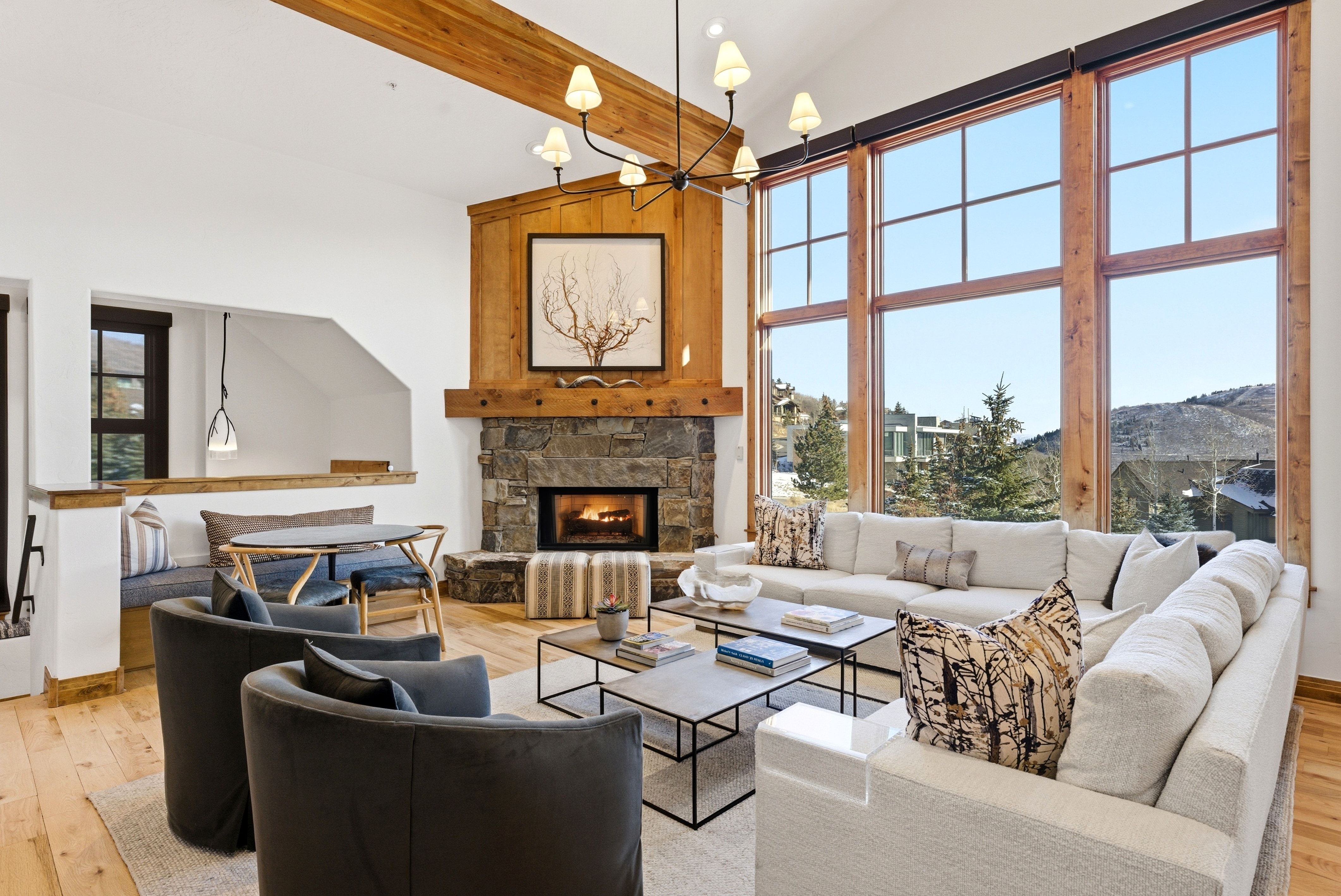 Spacious living area featuring a stone fireplace with a wood mantel, high vaulted ceilings with exposed wood beams, and a large wall of windows