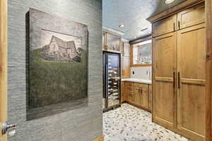 Kitchen with beverage cooler, wood finish cabinetry, a textured ceiling, light countertops, and recessed lighting