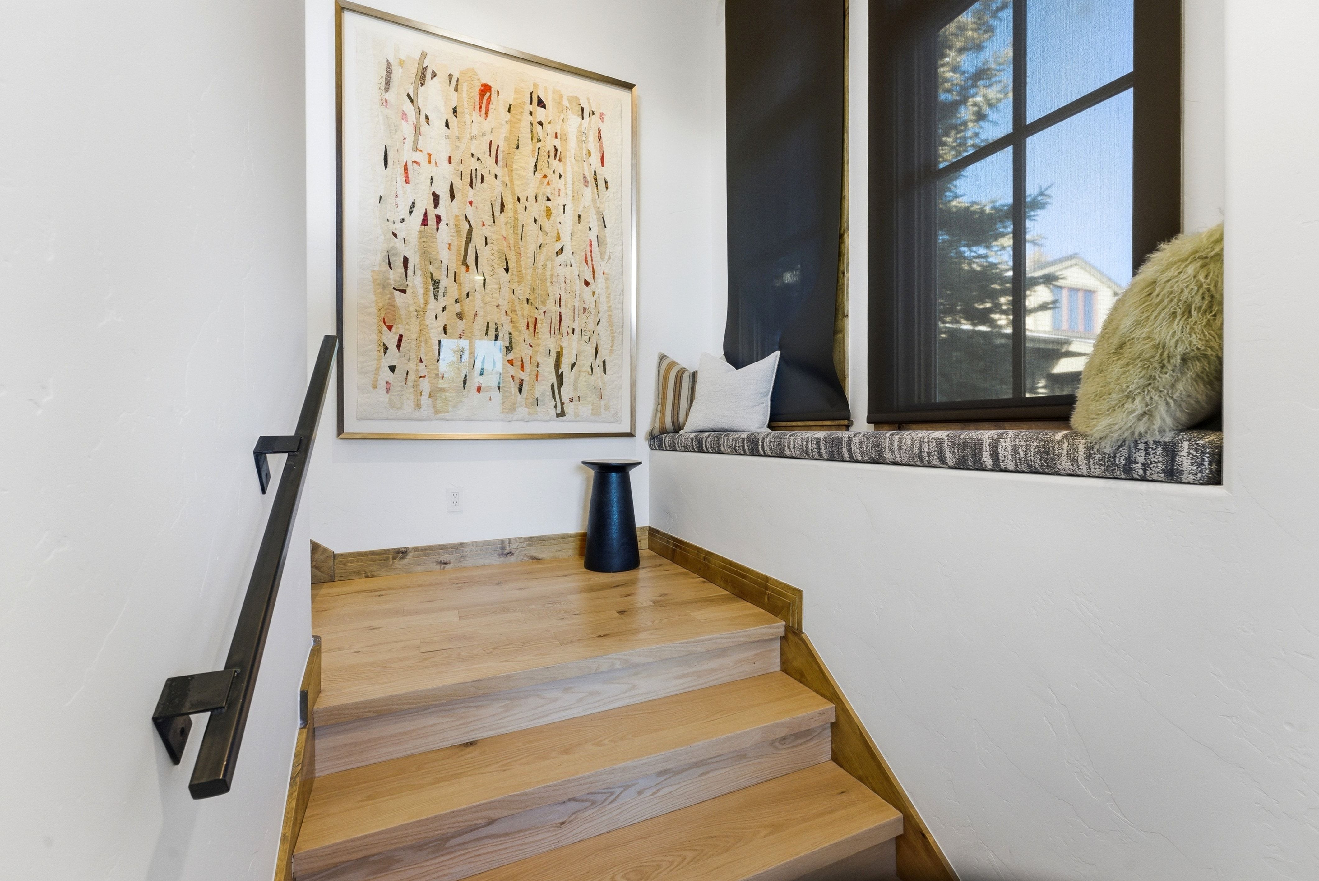 Staircase featuring wood-finish flooring, a contemporary black metal handrail, and a built-in window seat