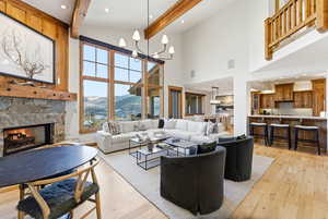 Living area with a mountain view, light wood finished floors, a chandelier, a stone fireplace, and beamed ceiling