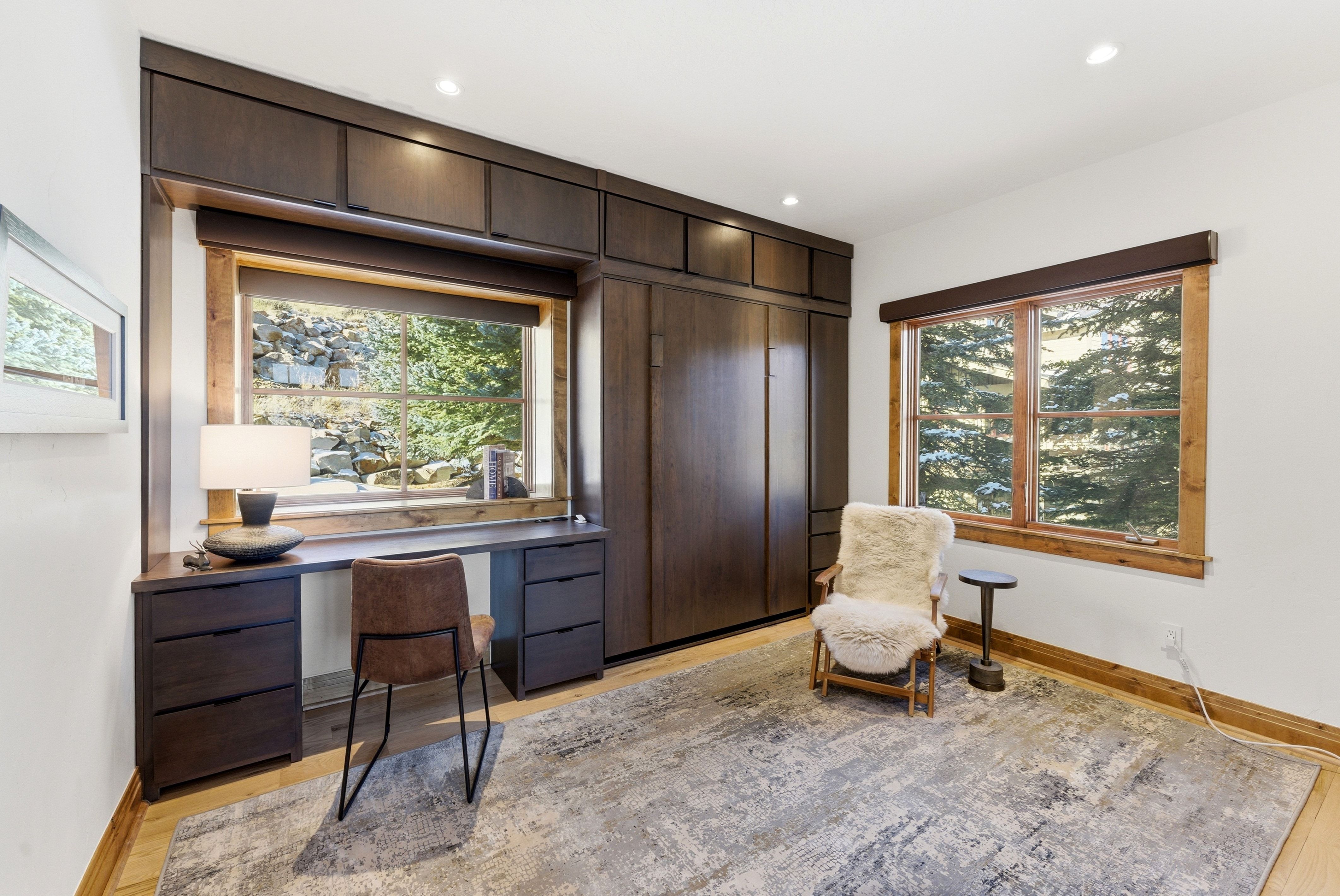 Built-in wood-finish desk with integrated drawers, wood-finish wall bed cabinetry, recessed lighting, wood-trimmed windows, and wood-finish flooring