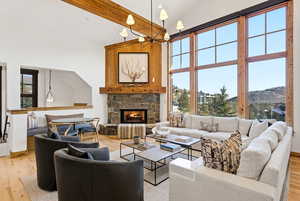 Living room with light wood-style flooring, a stone fireplace, lofted ceiling, and hanging lights