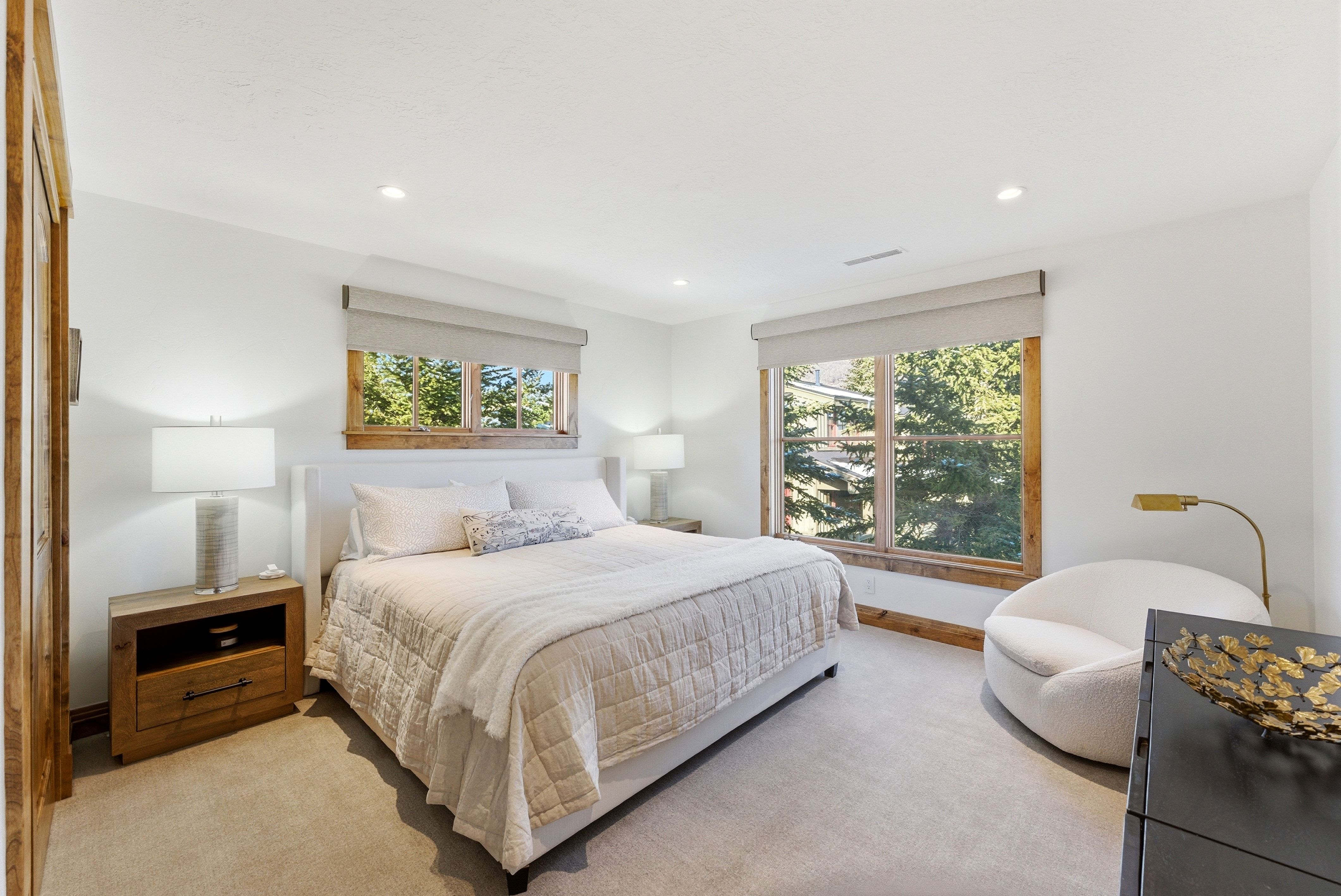 Carpeted bedroom featuring a large window with wood trim, recessed lighting, and a white upholstered bed frame