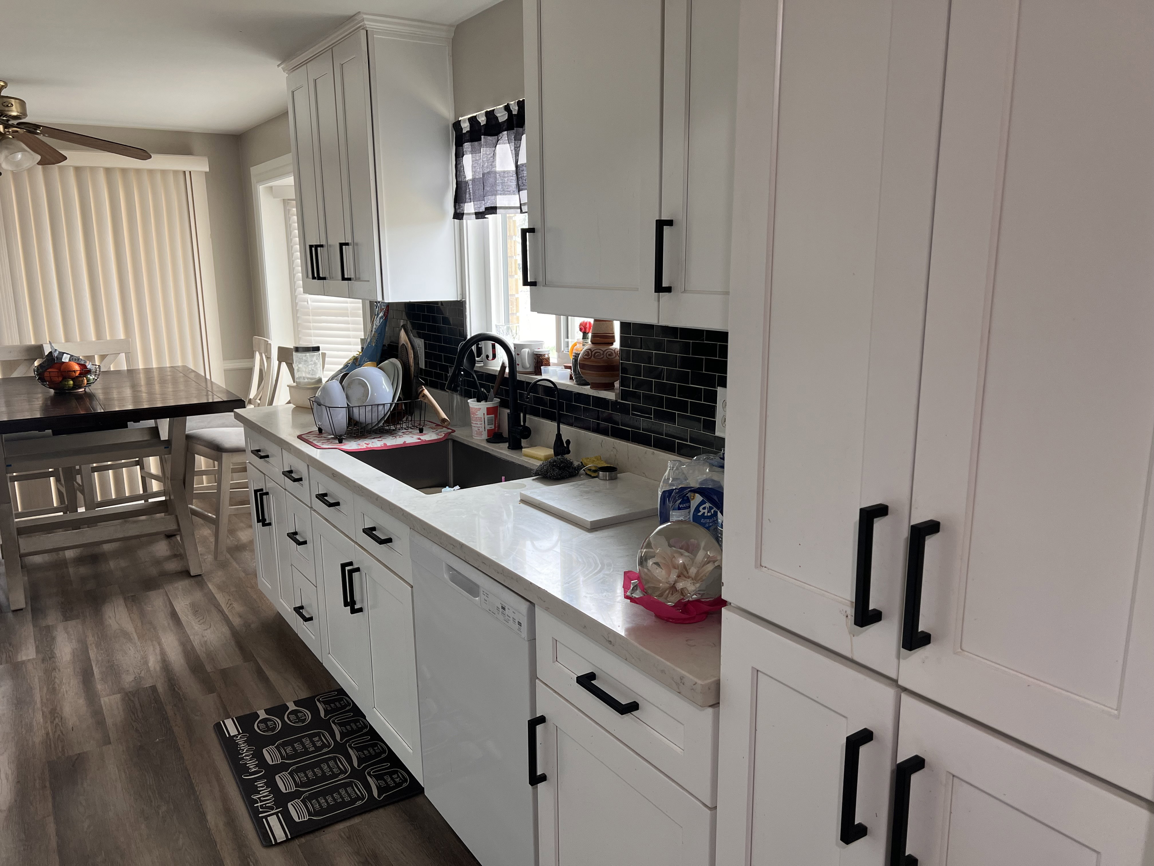 Kitchen with white dishwasher, a ceiling fan, white cabinets, dark wood-type flooring, and decorative backsplash