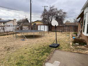 Fenced backyard featuring a storage unit and a trampoline