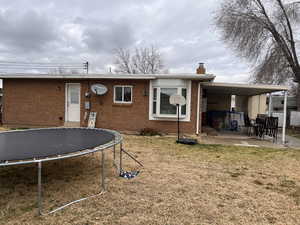 Rear view of property with a yard, a patio, a trampoline, a chimney, and brick siding