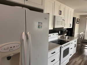 Kitchen featuring white appliances, white cabinets, dark wood-style floors, and tasteful backsplash