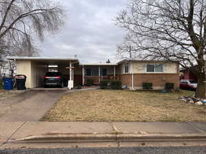 Ranch-style home featuring brick siding, concrete driveway, a front yard, an attached carport, and a porch