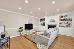 Living area featuring a warm lit fireplace, ornamental molding, light wood finished floors, recessed lighting, and built in features