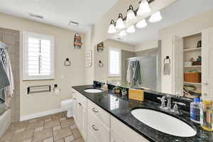 Bathroom featuring double vanity, bath / shower combo with glass door, and light stone finish flooring