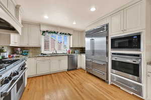 Kitchen with light stone counters, built in appliances, a warming drawer, light wood-style floors, and recessed lighting