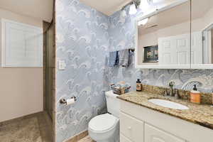 Bathroom with vanity, wallpapered walls, and a stall shower