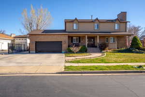 View of front of house with a porch, concrete driveway, an attached garage, brick siding, and a chimney
