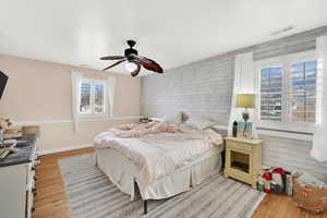 Bedroom with wood walls, a ceiling fan, light wood finished floors, and an accent wall