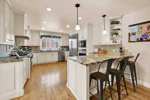 Kitchen featuring light stone countertops, a peninsula, hanging light fixtures, and a kitchen breakfast bar