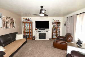 Living room featuring carpet, a textured ceiling, ceiling fan, and a fireplace