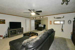 Living room with ornamental molding, carpet flooring, a ceiling fan, wallpapered walls, and a textured ceiling