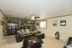 Carpeted living room featuring crown molding, a textured ceiling, ceiling fan, wallpapered walls, and a fireplace