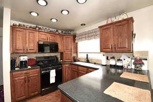 Kitchen featuring dark countertops, black appliances, wood finish cabinets, decorative backsplash, and light wood-style floors