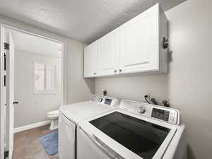 Laundry area with cabinet space, washing machine and dryer, light tile patterned floors, and a textured ceiling