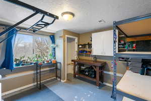 Miscellaneous room with a workshop area, a textured ceiling, and concrete floors