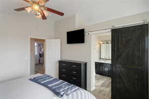 Bedroom with a barn door, vaulted ceiling, a ceiling fan, and ensuite bathroom