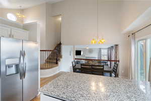 Kitchen featuring suspended lighting, stainless steel fridge, white cabinetry, light wood finished floors, and light stone counters