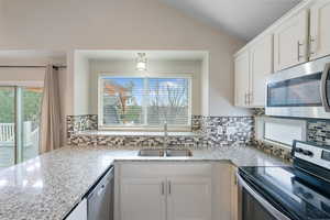 Kitchen with stainless steel appliances, light stone counters, white cabinets, vaulted ceiling, and a peninsula