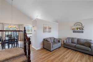 Living room featuring vaulted ceiling, suspended lighting, and light wood-style flooring