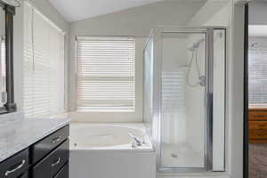 Full bathroom featuring a stall shower, a garden tub, vanity, and lofted ceiling