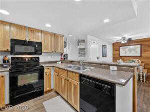 Kitchen featuring a peninsula, black appliances, light wood-style flooring, light countertops, and wood walls