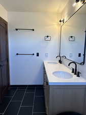 Full bath featuring double vanity, a textured ceiling, and dark tile patterned floors