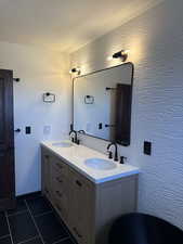 Bathroom with double vanity, dark tile patterned floors, and a textured ceiling