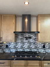 Kitchen with gas stovetop, light wood finish cabinetry, a textured ceiling, dark stone counters, and tasteful backsplash