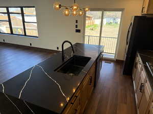 Kitchen with dark wood-style floors, freestanding refrigerator, hanging light fixtures, and healthy amount of natural light
