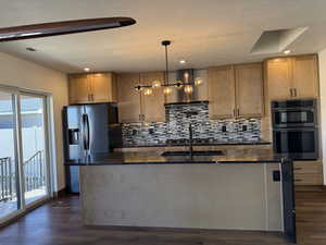 Kitchen featuring double oven, hanging light fixtures, decorative backsplash, a center island with sink, and a textured ceiling