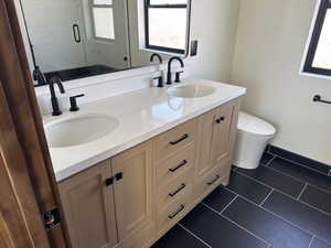 Full bath with double vanity and dark tile patterned flooring