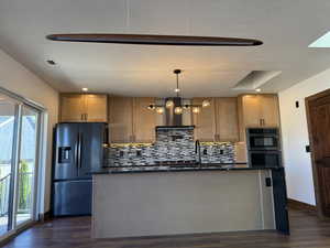 Kitchen with fridge with ice dispenser, hanging light fixtures, a center island with sink, and dark wood finished floors