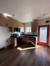 Kitchen featuring dark countertops, black appliances, dark wood-type flooring, and recessed lighting