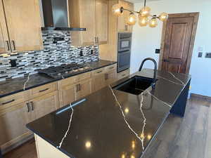 Kitchen featuring an island with sink, dark wood-style floors, dark stone countertops, and stainless steel gas cooktop
