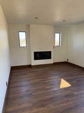 Unfurnished living room featuring a glass covered fireplace, dark wood finished floors, a textured ceiling, and recessed lighting