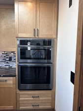 Kitchen view of double oven, light wood finish cabinets, and dark stone counters