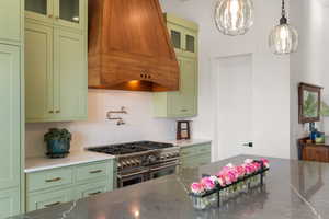 Kitchen featuring green cabinets, dark stone countertops, glass insert cabinets, range with two ovens, and decorative backsplash