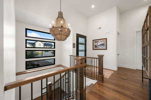Corridor with an upstairs landing, dark wood-style flooring, a chandelier, and vaulted ceiling