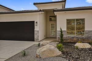 Entrance to property featuring stone siding, concrete driveway, stucco siding, an attached garage, and a tile roof